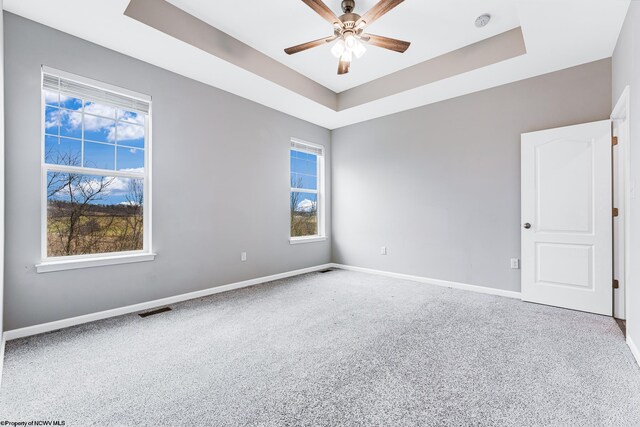 empty room with ceiling fan, a tray ceiling, and carpet floors