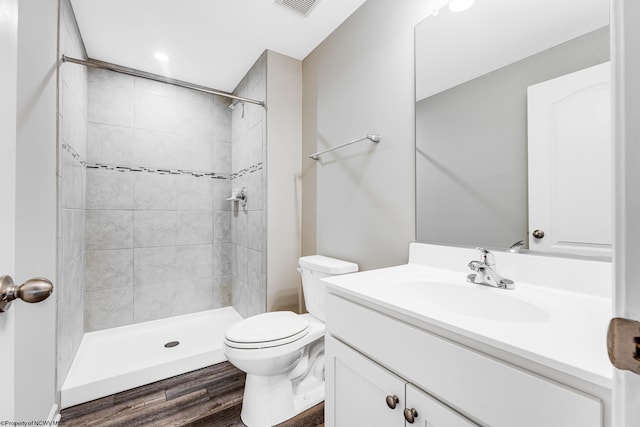 bathroom featuring vanity, wood-type flooring, toilet, and tiled shower