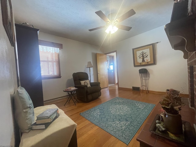 living room with ceiling fan, wood-type flooring, and a textured ceiling