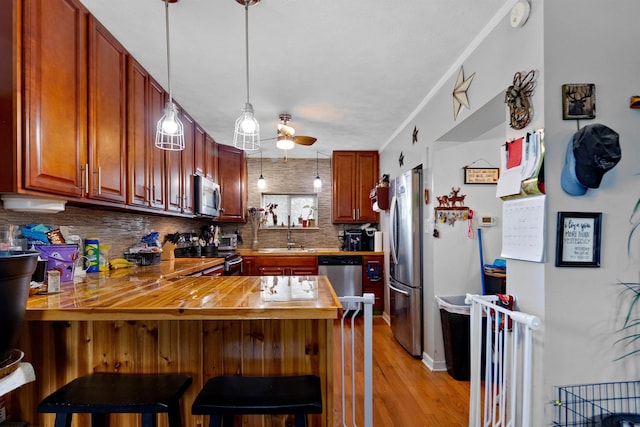 kitchen featuring a kitchen bar, hanging light fixtures, appliances with stainless steel finishes, kitchen peninsula, and backsplash