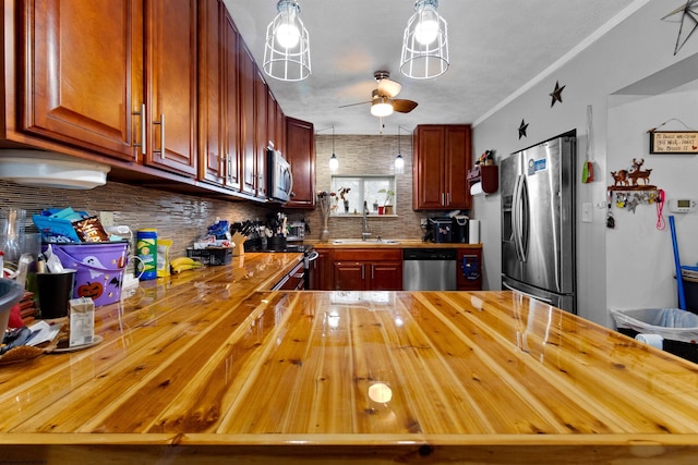 kitchen with pendant lighting, butcher block countertops, sink, stainless steel appliances, and tasteful backsplash