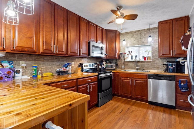 kitchen with appliances with stainless steel finishes, wood counters, sink, hanging light fixtures, and light hardwood / wood-style floors