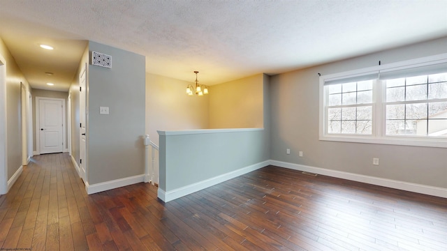 unfurnished room featuring dark wood-type flooring, an inviting chandelier, and a textured ceiling