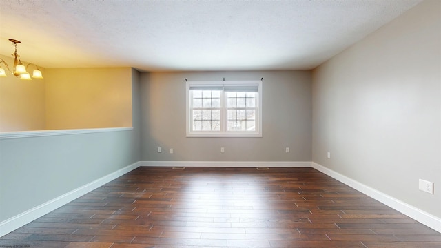 spare room featuring a textured ceiling, dark hardwood / wood-style floors, and a chandelier