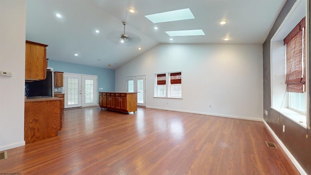 unfurnished living room featuring high vaulted ceiling, a skylight, ceiling fan, dark wood-type flooring, and french doors