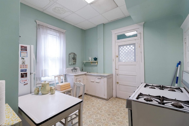 kitchen with white appliances, white cabinetry, sink, and a paneled ceiling