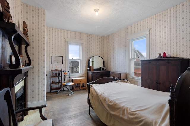 bedroom featuring light hardwood / wood-style floors, multiple windows, a textured ceiling, and a fireplace