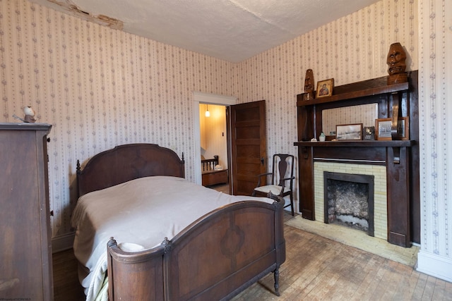 bedroom featuring hardwood / wood-style floors, a textured ceiling, and a brick fireplace