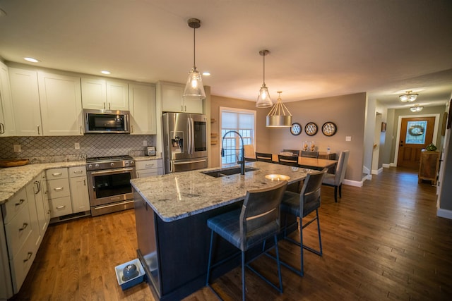 kitchen featuring appliances with stainless steel finishes, an island with sink, light stone counters, pendant lighting, and sink