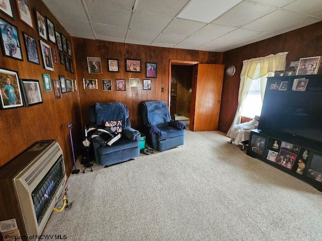 living area with heating unit, wood walls, a paneled ceiling, and carpet