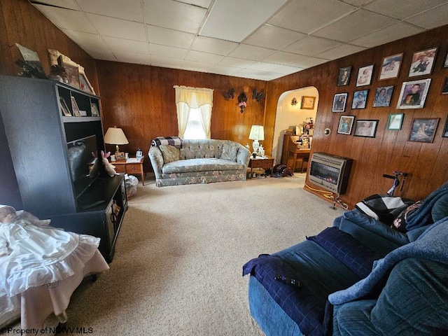 carpeted living room with heating unit, wood walls, and a drop ceiling