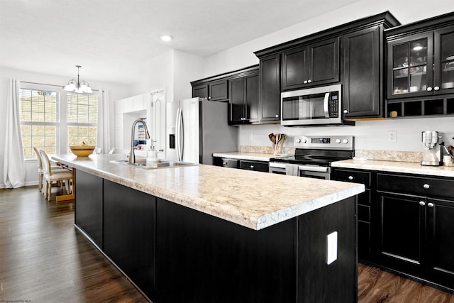 kitchen featuring a center island with sink, stainless steel appliances, light countertops, glass insert cabinets, and dark cabinetry