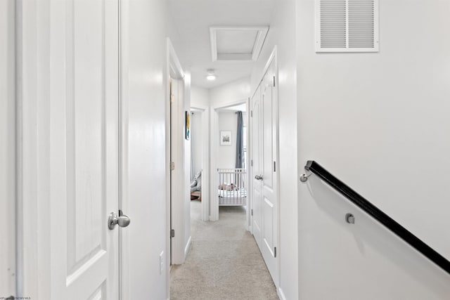 corridor with light carpet, visible vents, attic access, and baseboards