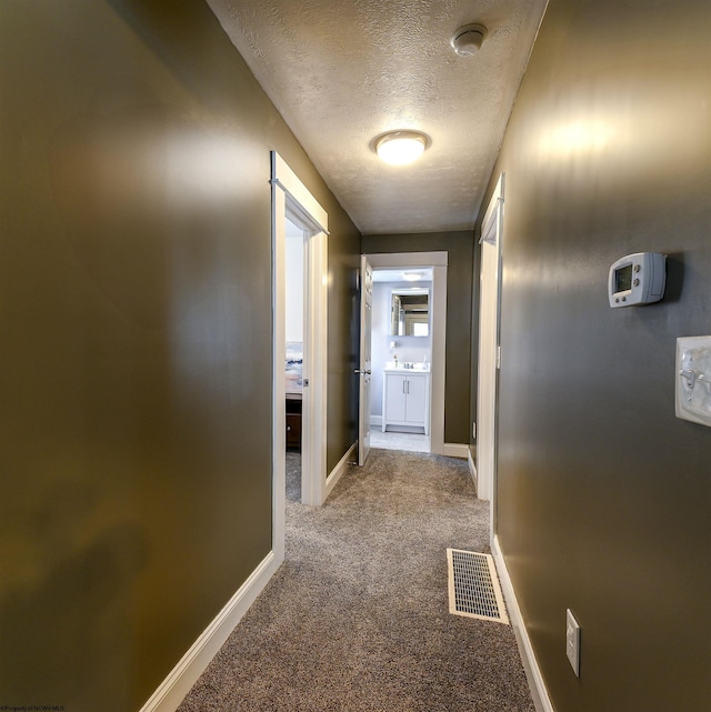 hall featuring a textured ceiling, carpet flooring, visible vents, and baseboards