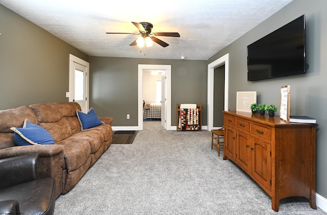 living area with a ceiling fan, light carpet, a textured ceiling, and baseboards