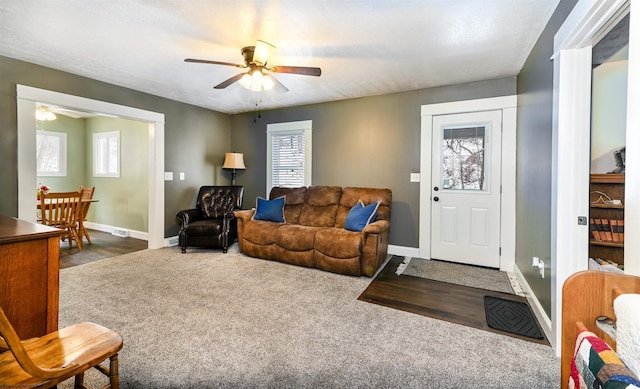 carpeted living area with ceiling fan and baseboards