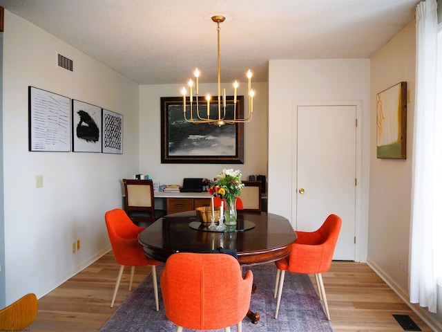 dining area featuring visible vents, light wood-style flooring, and an inviting chandelier