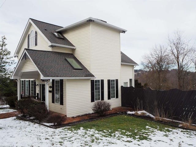 snow covered property with a shingled roof and fence