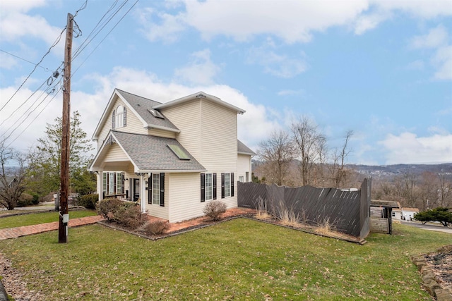 view of side of home featuring a shingled roof, fence, and a lawn