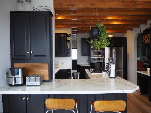 kitchen featuring arched walkways, appliances with stainless steel finishes, light stone countertops, a peninsula, and a kitchen breakfast bar