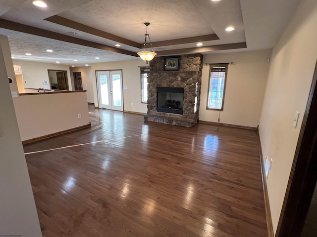 unfurnished living room featuring dark wood-style floors, plenty of natural light, a raised ceiling, and a stone fireplace