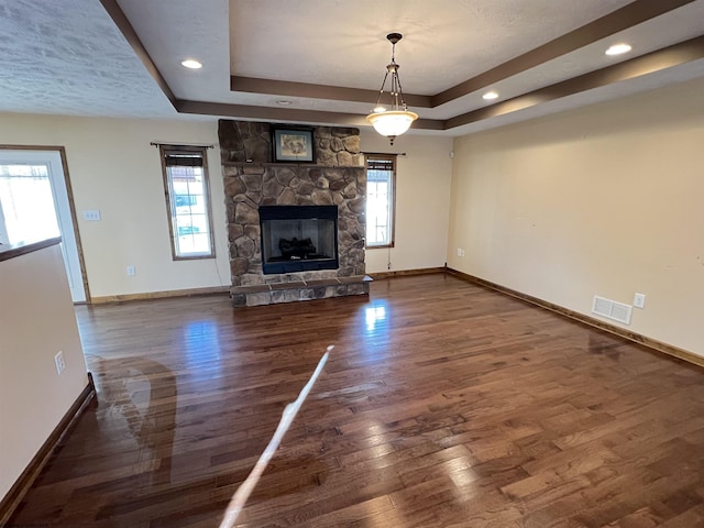 unfurnished living room with a tray ceiling, dark wood-style flooring, visible vents, and baseboards