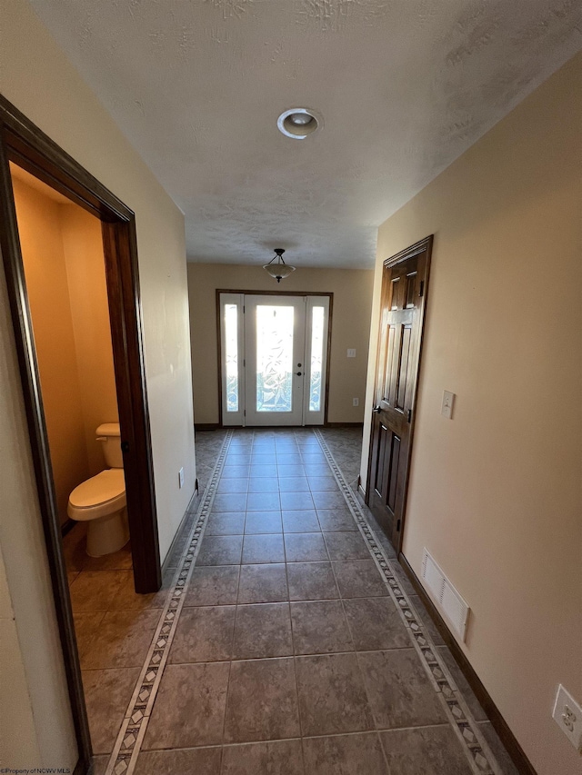 doorway with baseboards, visible vents, a textured ceiling, and dark tile patterned flooring