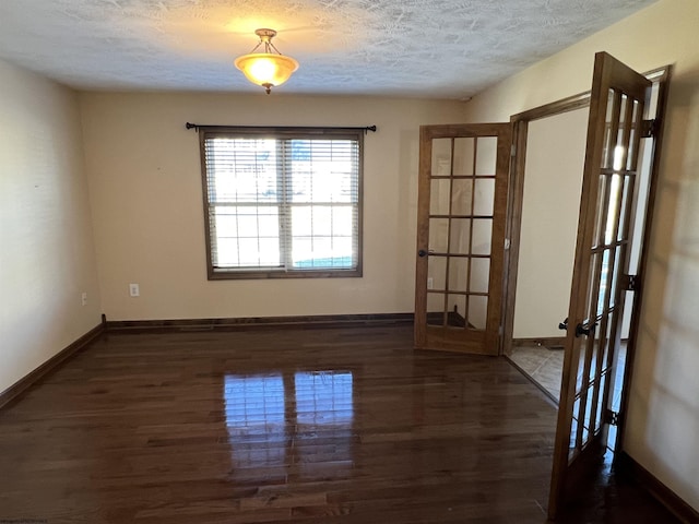 empty room with dark wood-type flooring, french doors, a textured ceiling, and baseboards