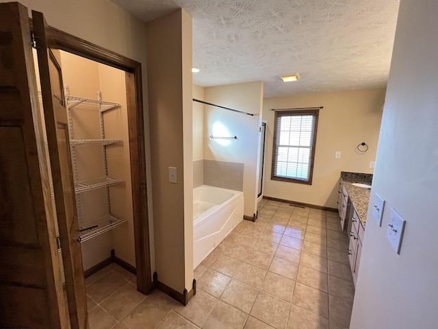 full bathroom with a garden tub, a spacious closet, a textured ceiling, and vanity