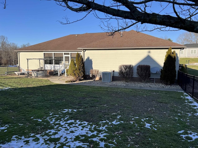 rear view of house with central air condition unit, a sunroom, fence, and a lawn