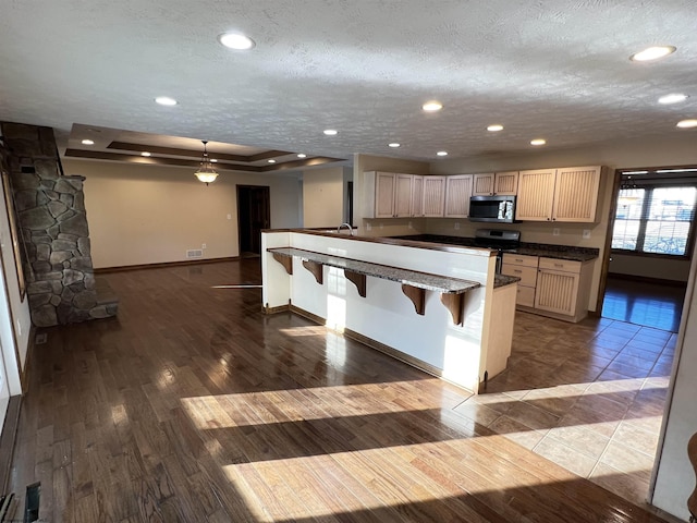 kitchen with a textured ceiling, a breakfast bar, wood finished floors, open floor plan, and hanging light fixtures