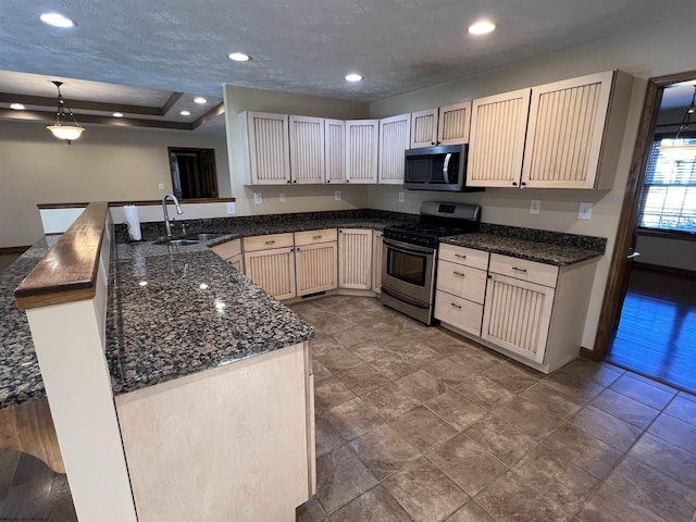 kitchen featuring pendant lighting, stainless steel appliances, a sink, dark stone countertops, and a peninsula