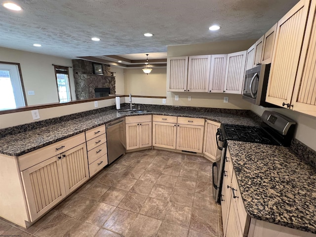 kitchen featuring a textured ceiling, a peninsula, a sink, hanging light fixtures, and appliances with stainless steel finishes