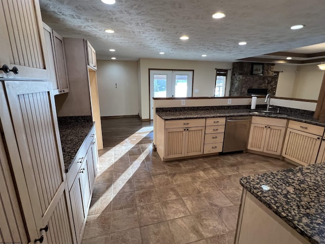 kitchen with stainless steel dishwasher, open floor plan, a sink, a textured ceiling, and a peninsula