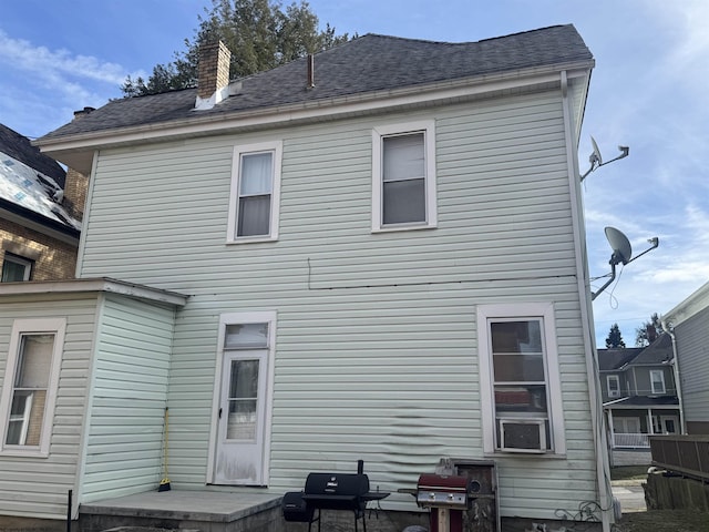 rear view of house with roof with shingles and a chimney