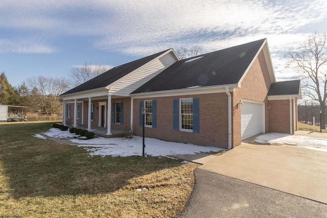 view of side of property featuring brick siding, a yard, covered porch, an attached garage, and driveway