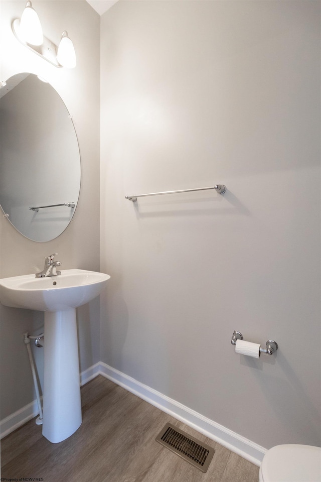 half bath featuring baseboards, visible vents, and wood finished floors