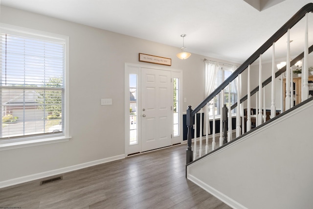 foyer entrance with stairs, dark wood finished floors, visible vents, and a healthy amount of sunlight