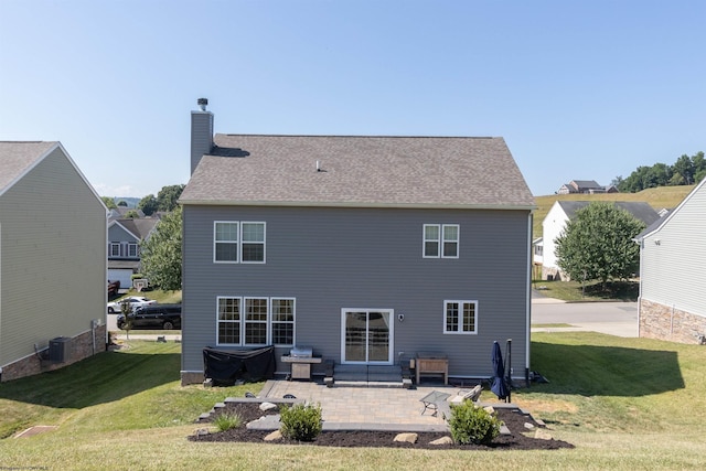 rear view of property featuring roof with shingles, a patio, a chimney, and a lawn