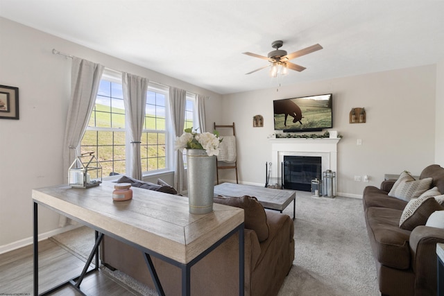 living area featuring a fireplace with flush hearth, baseboards, a ceiling fan, and carpet flooring