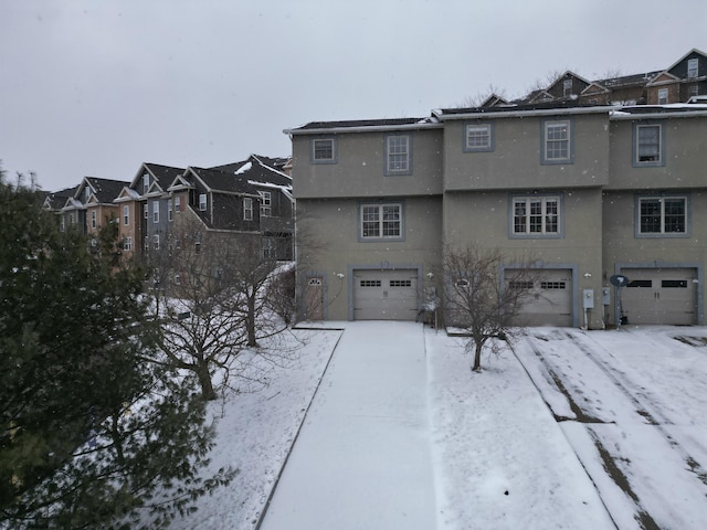 snow covered house featuring an attached garage, a residential view, and stucco siding