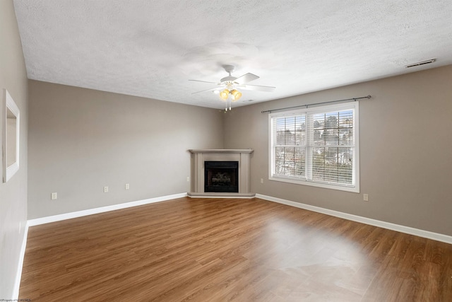 unfurnished living room with ceiling fan, baseboards, a fireplace with raised hearth, and wood finished floors