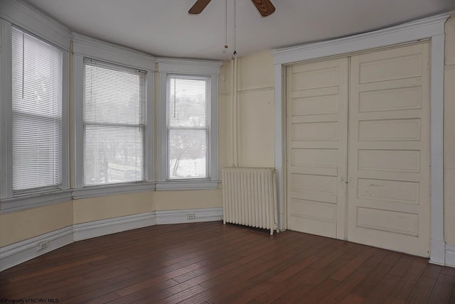 unfurnished bedroom featuring radiator, a closet, multiple windows, and dark wood-type flooring