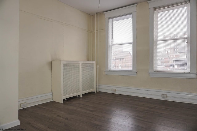 empty room featuring baseboards, dark wood-style flooring, and radiator