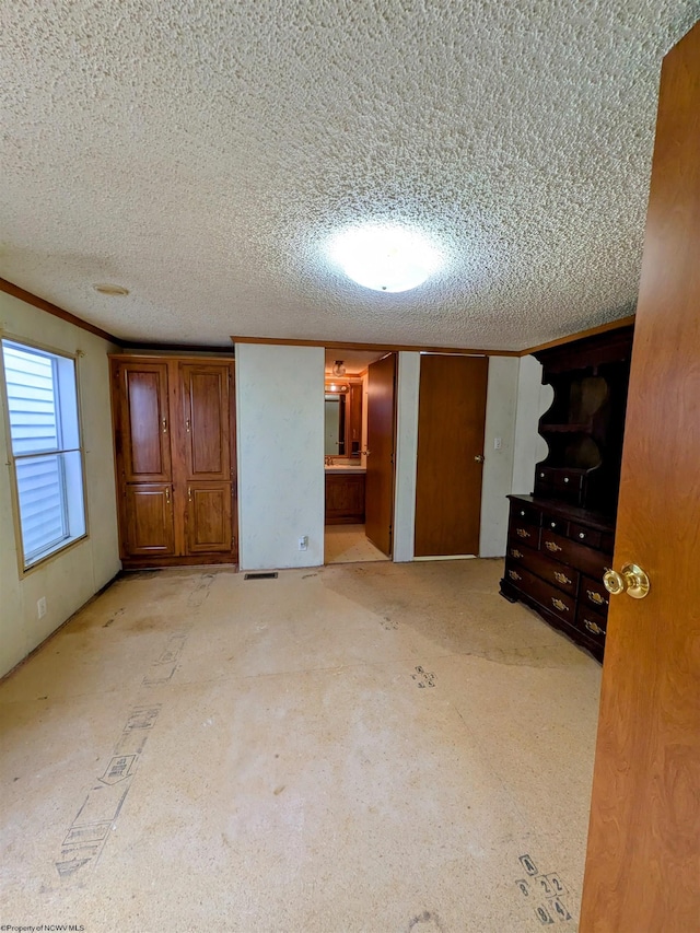 unfurnished bedroom with ensuite bath, crown molding, and a textured ceiling