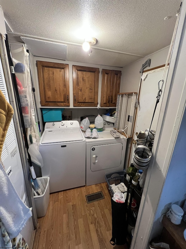 laundry area with cabinet space, light wood finished floors, a textured ceiling, and independent washer and dryer