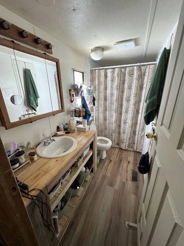 full bathroom with a textured ceiling, toilet, wood finished floors, vanity, and visible vents