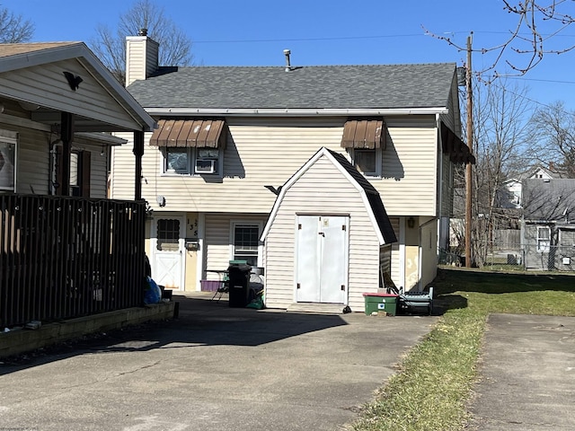 view of front facade featuring a shingled roof, a chimney, and fence