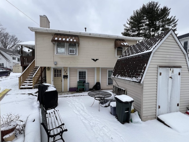 snow covered property with a chimney, stairway, and a gambrel roof