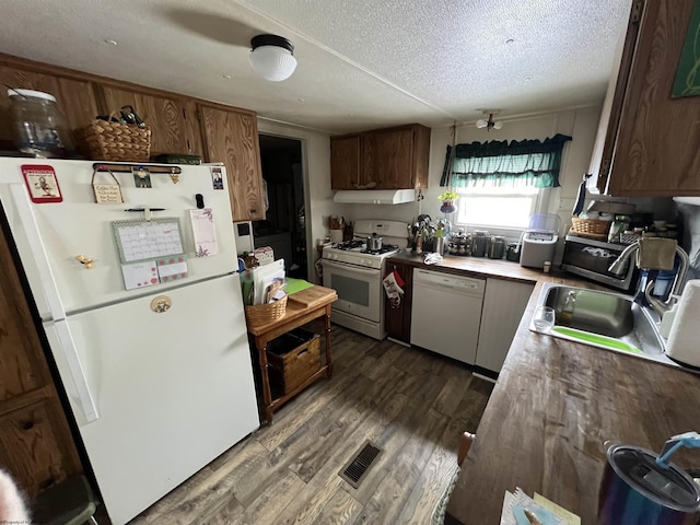 kitchen with under cabinet range hood, white appliances, visible vents, light countertops, and dark wood-style floors